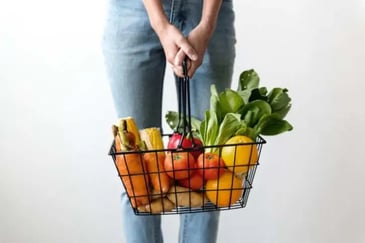 A young person carrying a basket full of fruits and vegetables