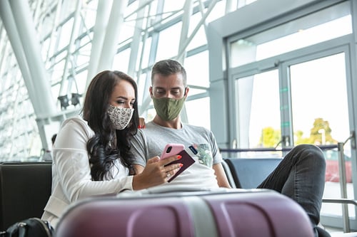 Couple with masks at airport look at smartphone