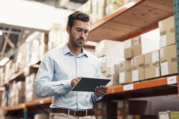 Male merchandise planner doing stock inventory in warehouse with tablet