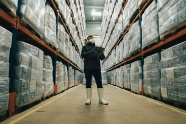 Merchant doing stock inventory in a warehouse using a tablet while wearing safety equipment