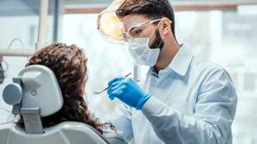 Male dentist performing dental cleaning on female patient