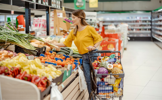 Female shopper grabbing vegetables to add to full shopping cart