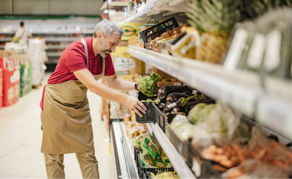 Male grocery employee stocking shelves in produce aisle