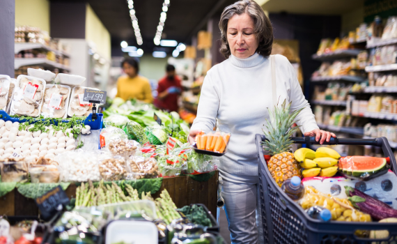 Senior female shopper adding vegetables to full grocery cart