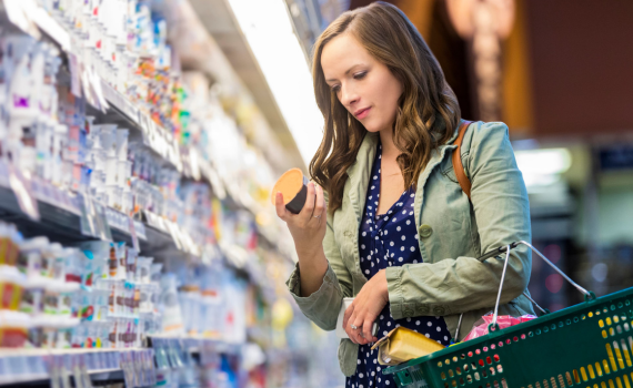 Woman at grocery store reading food labels while holding her shopping basket