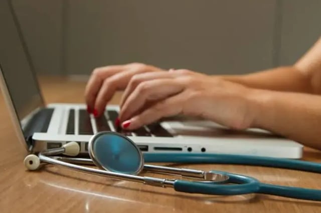 Healthcare professional using laptop with stethoscope laying on desk