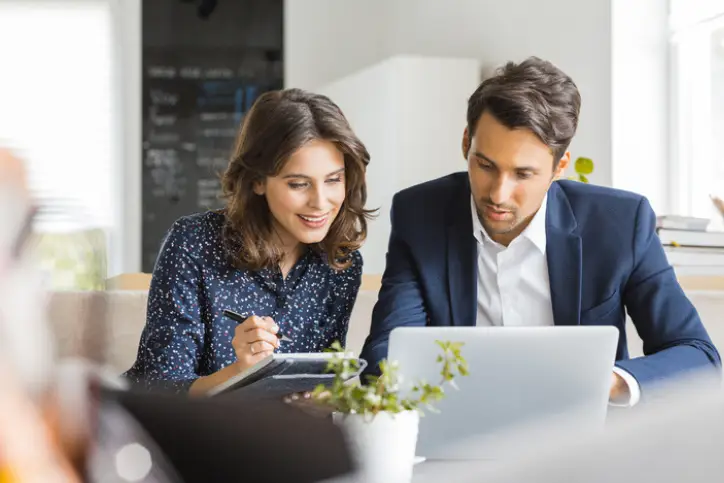 Male and female insurance colleagues collaborating in office using AI laptop