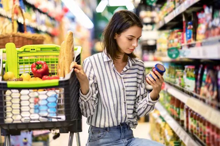 Woman with full grocery cart checking the price of a product in the grocery store