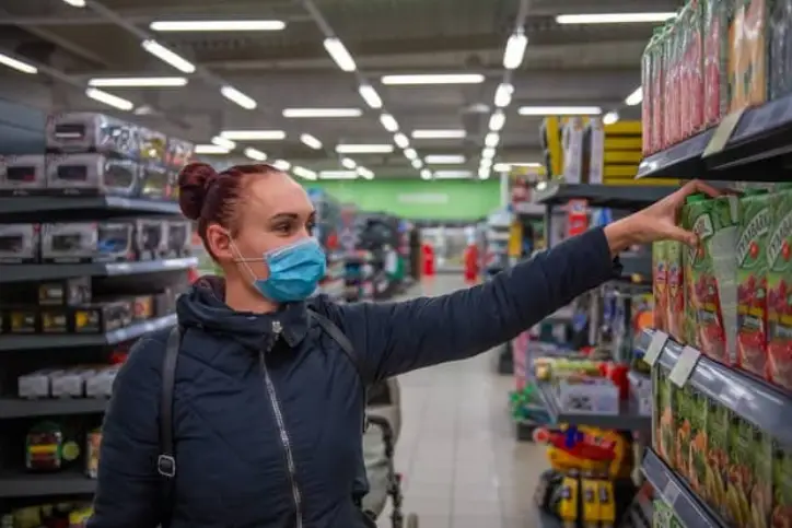lady in mask picking out a product in grocery shop aisle
