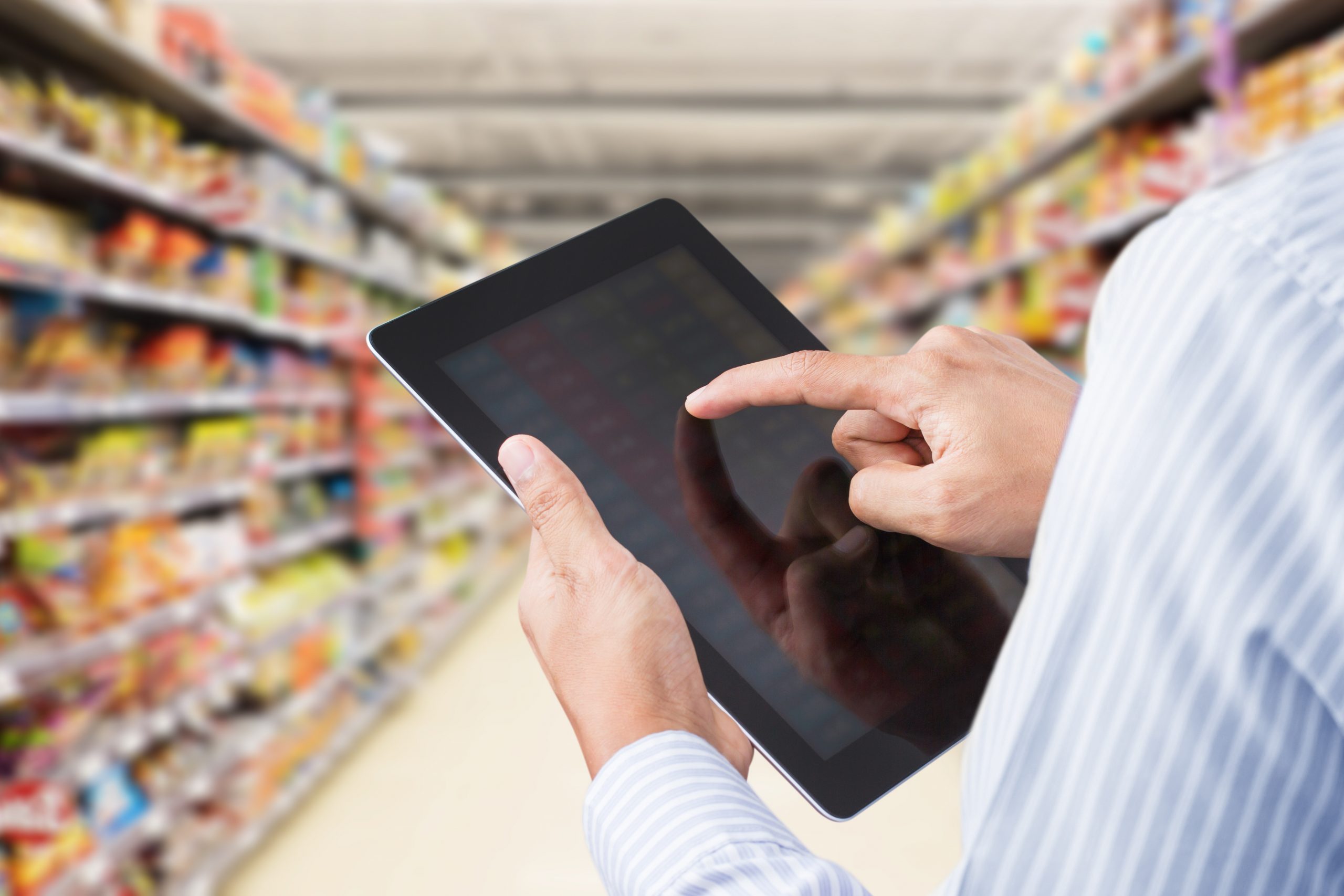 Male grocery merchant using tablet in grocery aisle